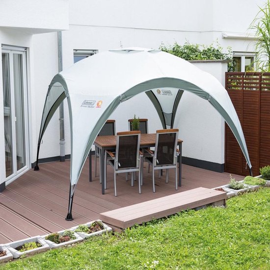 Grijze partytent met gebogen poten, geplaatst op een houten terras met tafel en stoelen.