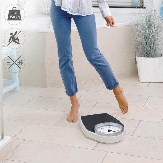 Personne en jean bleu montant sur une balance analogique dans une salle de bain.