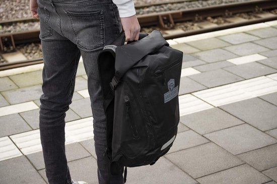Man draagt zwarte waterdichte Undercover Dsign rugzak met logo op perron.