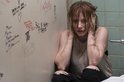 Vrouw met rood haar, de handen over de oren, zittend op de grond voor een muur met graffiti.