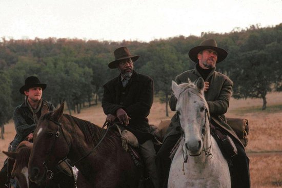 Morgan Freeman, Clint Eastwood en een andere man te paard in een landelijke omgeving bij zonsondergang.