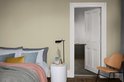 Slaapkamer met gestyled bed, bijzettafel en een oranje fauteuil, naast een open badkamerdeur.