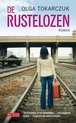 Een vrouw met spijkerbroek en beige jas staat op spoorrails met een oranje koffer.