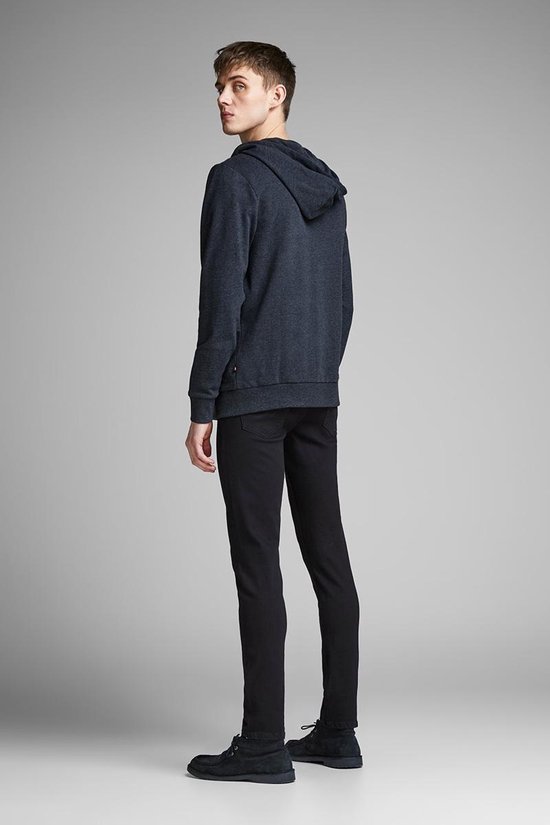 Model draagt een donkerblauwe hoodie met rits en een zwarte jeans.