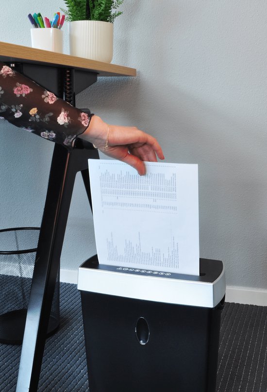 Hand voegt papier toe aan zwarte papierversnipperaar met zilveren bovenkant.