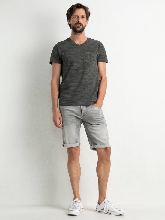 Man met een grijze gestreepte T-shirt en grijze denim shorts. Hij draagt witte sneakers.