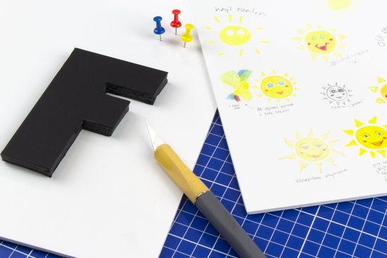 Zwarte letter F van schuimplaat naast schetsen van zonnetjes, met pushpins.