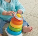 Close-up van een baby die speelt met een Fisher-Price stapelpiramide. Ze houdt een kleurrijke ring voor haar gezicht.