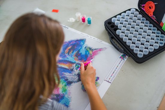 Une femme réalise une peinture diamantée d'un chat coloré avec un stylo rose.