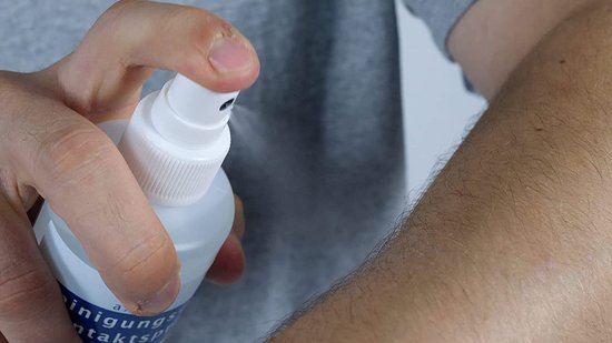 Hand spuit Axion kontaktspray op een behaarde huid.