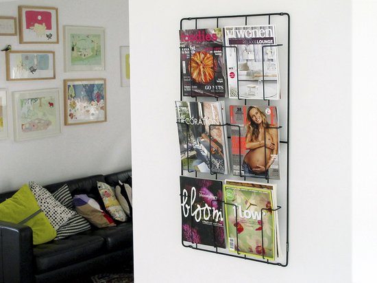 Zwart wandrek met 6 vakken, gevuld met diverse tijdschriften. Een zwarte bank staat ernaast.