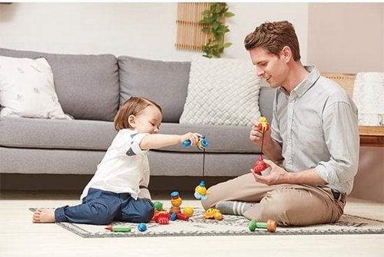 Een man en kind spelen op een kleed met magnetisch constructiespeelgoed, waaronder een vishengel.