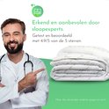 Vrolijke arts met stethoscoop wijst naar een opgevouwen witte zomerdekbed met groen bamboe bladpatroon.