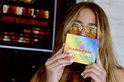 Vrouw met zonnebril houdt een Eargasm oordoppen Pride Edition doosje vast, met een regenboog ontwerp.