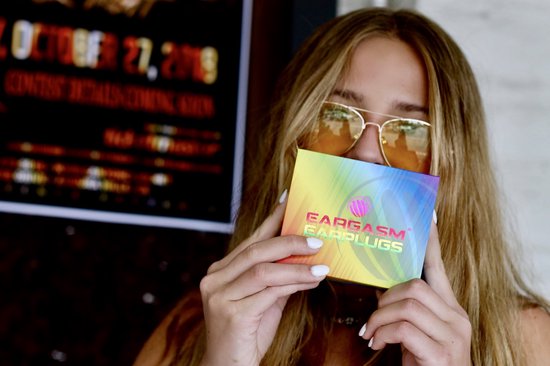 Vrouw met zonnebril houdt een Eargasm oordoppen Pride Edition doosje vast, met een regenboog ontwerp.