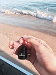 Hand op het strand houdt een Eargasm oordoppen koker en een sleutel vast met de oceaan op de achtergrond.