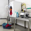 Een hydrofoorpomp met gele motorbehuizing naast een wasmachine met open deur, in een ruimte met proviand.
