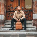 Man zittend op trappen met cognac leren rugzak, bij houten deur.