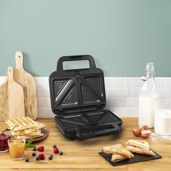 Zwart, open wafelijzer met driehoekige grillplaten. Broodjes en wafels op aanrecht.