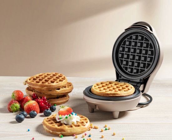 Gouden wafelijzer met een wafel en een stapel wafels. Ook fruit en decoraties.
