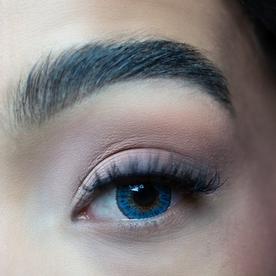Close-up van een oog met een helderblauwe contactlens en make-up.