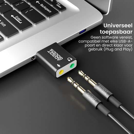 Zwarte USB-geluidskaartadapter met 3,5mm audioconnectoren, naast een laptop toetsenbord.