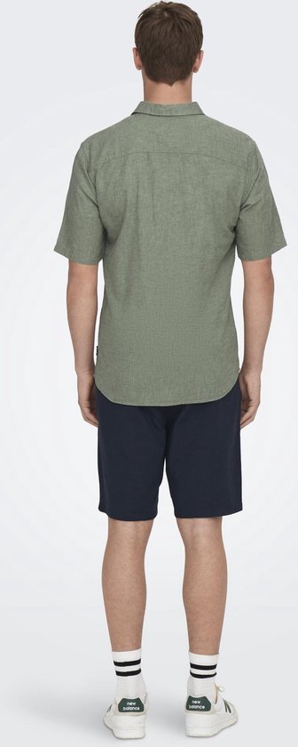Zicht op de achterkant van een man die een lichtgroen linnenmix overhemd met korte mouwen en donkerblauwe shorts draagt.