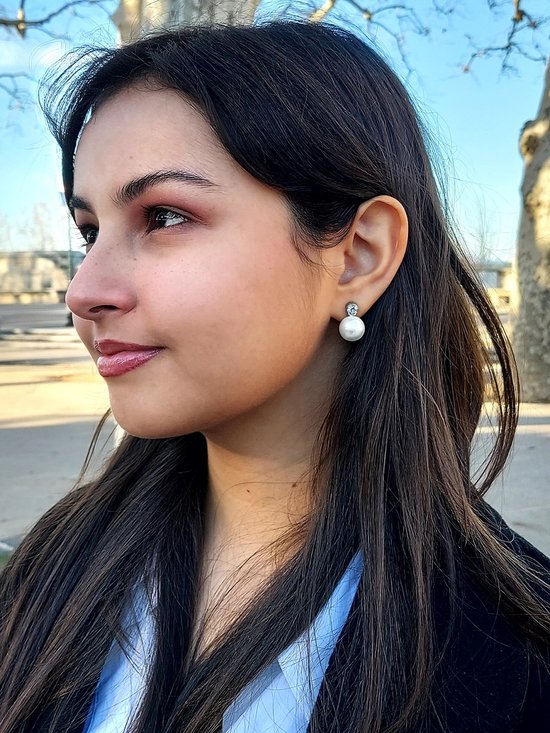 Model draagt een zilverkleurige clip-oorbel met een witte parel van 12 mm en een helder kristal.