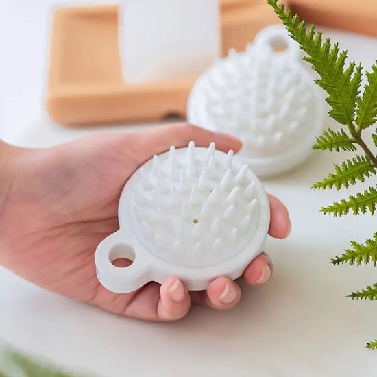 Witte hoofdhuidmassager met ronde siliconen nopjes, vastgehouden in een hand.