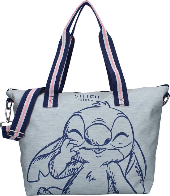 Tote bag en tissu bleu clair avec un grand dessin bleu marine de Stitch mettant son doigt dans sa bouche. Les anses sont rayées bleu marine, rose et blanc.