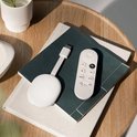 Witte Chromecast en afstandsbediening op een stapel boeken op een houten tafel.