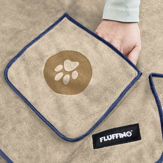 Close-up van een beige FLUFFINO hondenhandoek met een bruine pootafdruk in het midden en een hand die de hoek optilt.