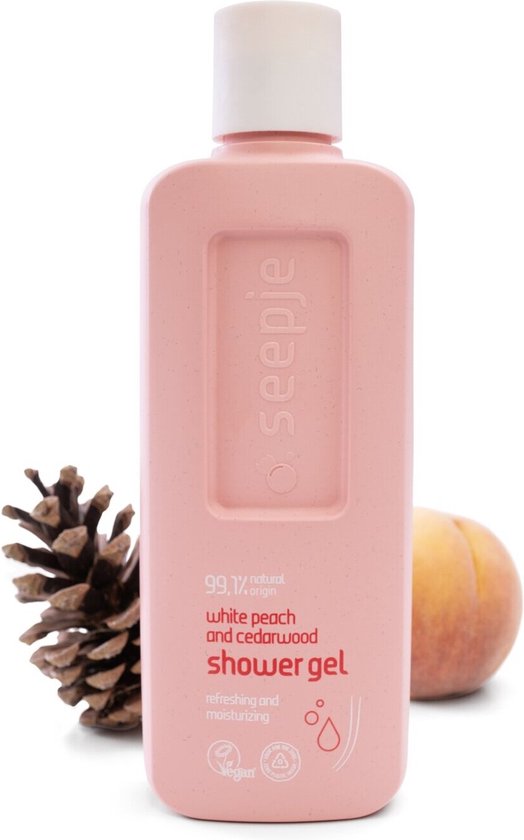 Roze fles Seepje douchegel met witte perzik en cederhout, naast een dennenappel en een perzik.