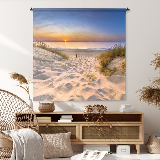 Wandkleed met duinlandschap en zonsondergang boven een houten dressoir in een modern interieur.