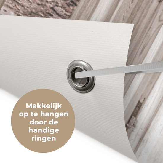 Detail van een tuinposter met een metalen ring voor eenvoudige bevestiging. Tekst: 'Makkelijk op te hangen door de handige ringen'.