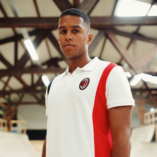 Man draagt een wit poloshirt met rode en zwarte strepen aan de zijkanten en het AC Milan-logo.