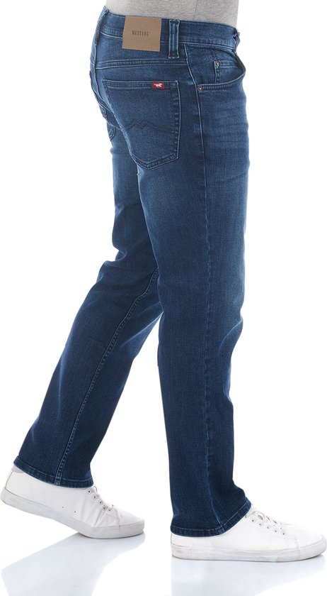 Zijaanzicht van een man in een donkerblauwe straight fit jeans, met het Mustang merklabel op de achterkant.