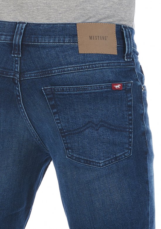 Detail van een donkerblauwe Mustang jeans met merklabel en paardenlogo op de achterzak.