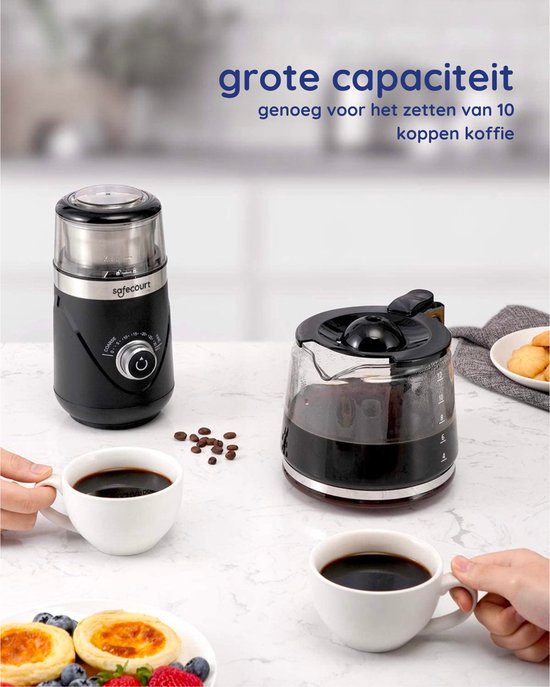 Zwarte Safecourt koffiemolen naast een koffiezetapparaat, met twee koppen koffie, koffiebonen en koekjes.