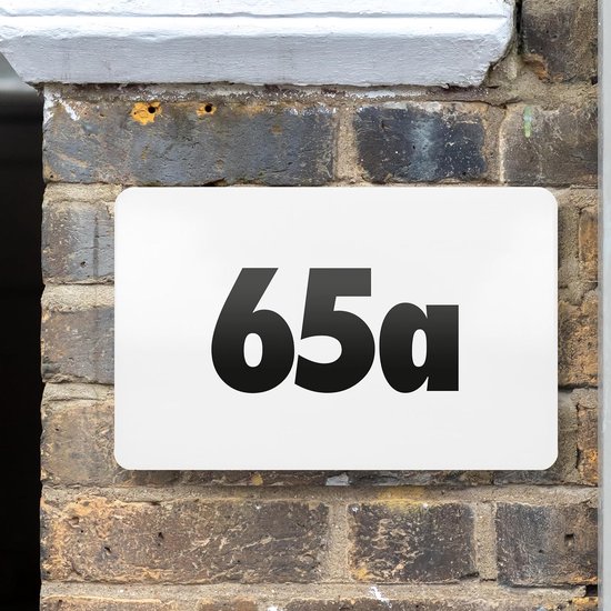 Verlichte witte huisnummerplaat '65a' gemonteerd op een bakstenen muur.