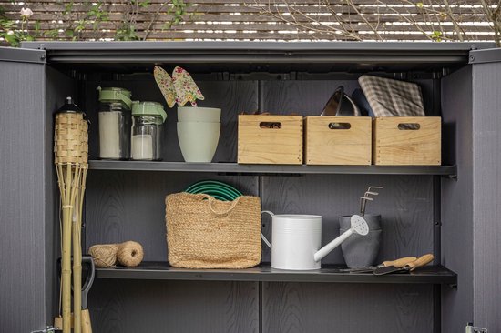 Binnenkant van bruine berging met planken, gevuld met tuinbenodigdheden zoals een gieter, manden en gereedschap.
