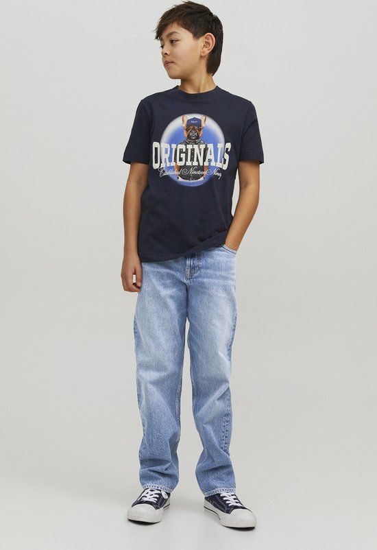 Jongen in donkerblauw T-shirt met hond-print, zittend in lichtblauwe jeans. Draagt sneakers.