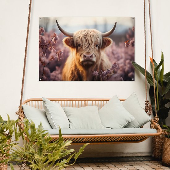 Een bruine Schotse hooglander met lange, golvende vacht staat in een veld met roze bloesems. De poster hangt aan een witte muur boven een hangbank.