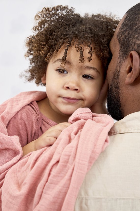 Kindje kijkt opzij, gewikkeld in een zachtroze swaddle, op de schouder van een man.