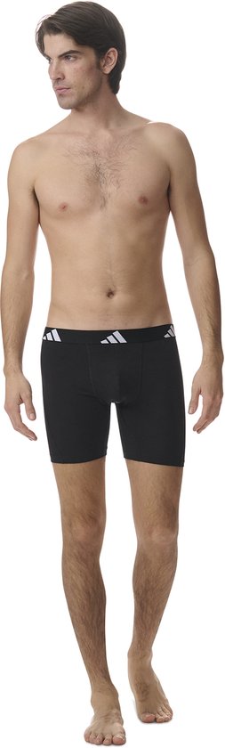 Man in zwarte Adidas boxer briefs met witte Adidas logo's op de tailleband.