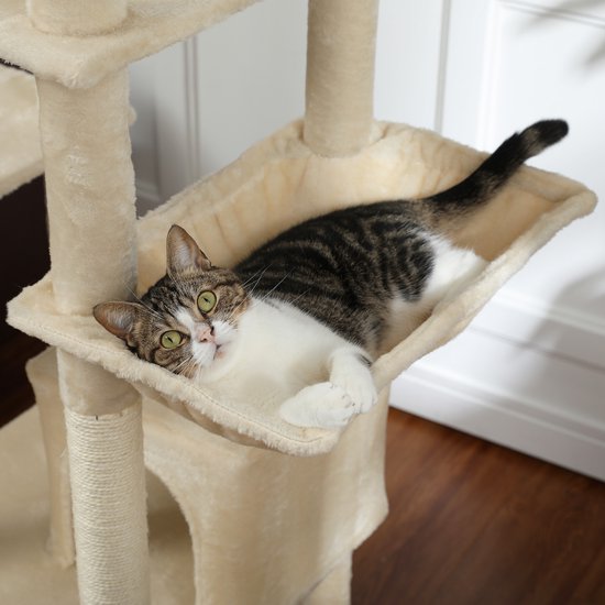 Een gestreepte tabby kat met witte borst en poten ligt in een crèmekleurige hangmat op een krabpaal.