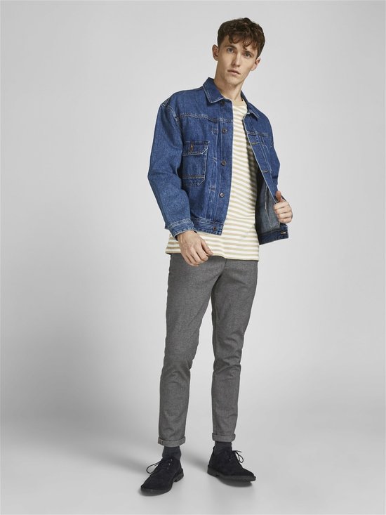 Model in grijze broek met visgraatpatroon, gestreepte top en spijkerjack.