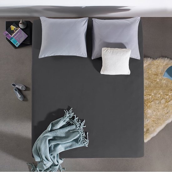 Donkergrijs hoeslaken op een bed, van bovenaf gezien. Beddengoed, plaid en vloerkleed.