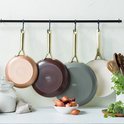 Vier koekenpannen met gouden handvatten hangen aan een rek. Kleuren: koper, bruin, grijs en crème.