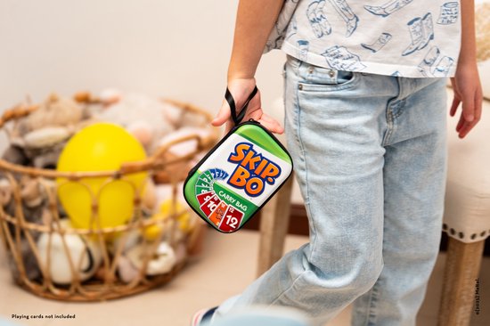 Een kind met spijkerbroek houdt een groene Skip-Bo draagtas vast met een zwart handvat.